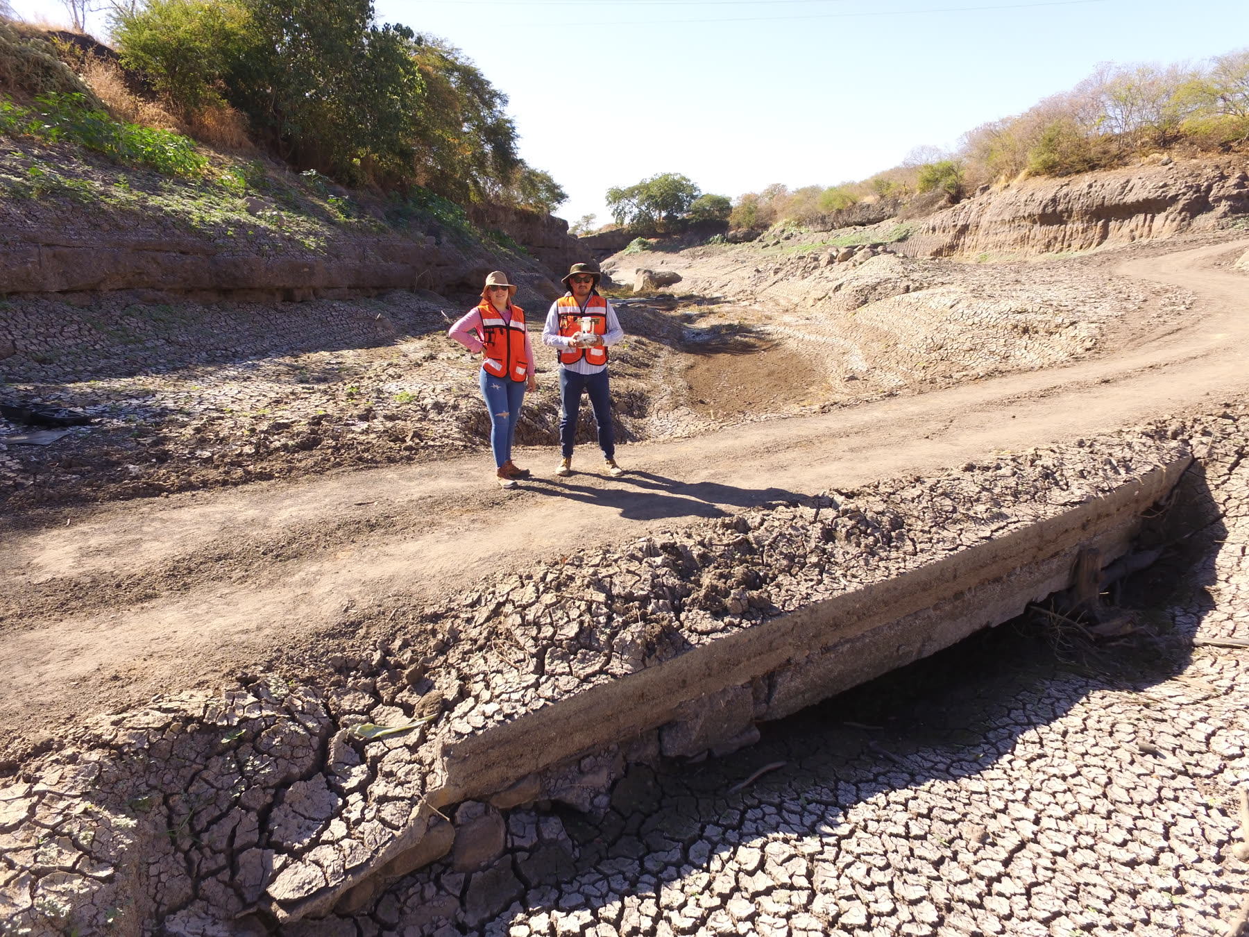 Two field staff in safety vests standing in a dry civil works channel