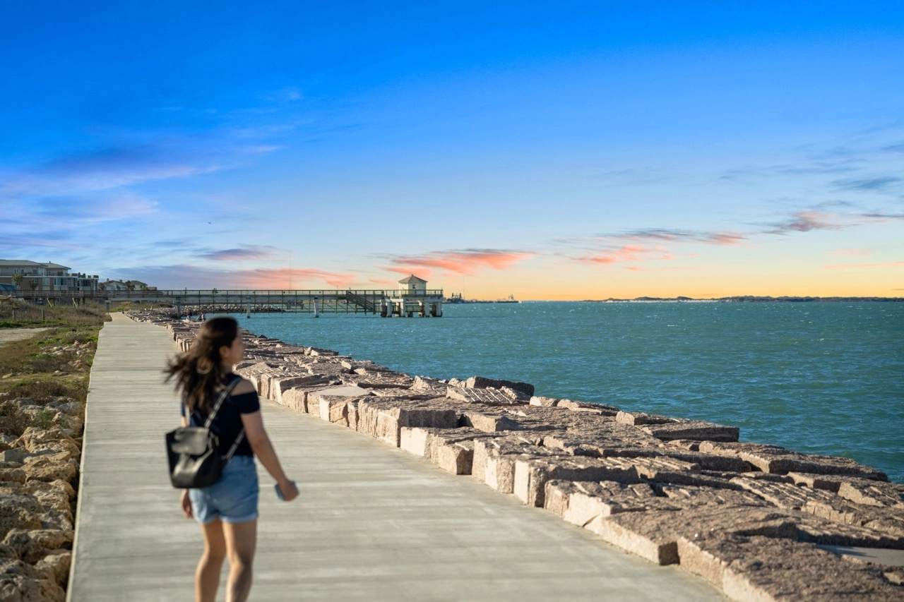 Person walking along a seawall beside the water at sunset