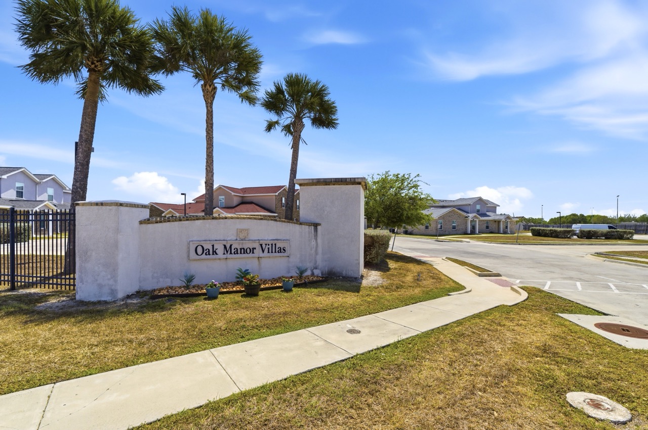 Stone sign for the 'Oak Manor Villas' community with manicured landscaping and palm trees, Portland, Texas