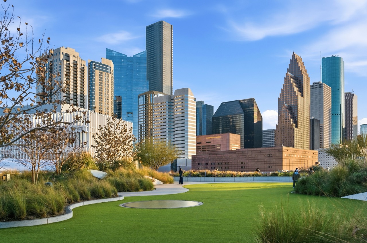 View of Discovery Green Park in Houston under a bright sky, with paths, trees, and the downtown skyline