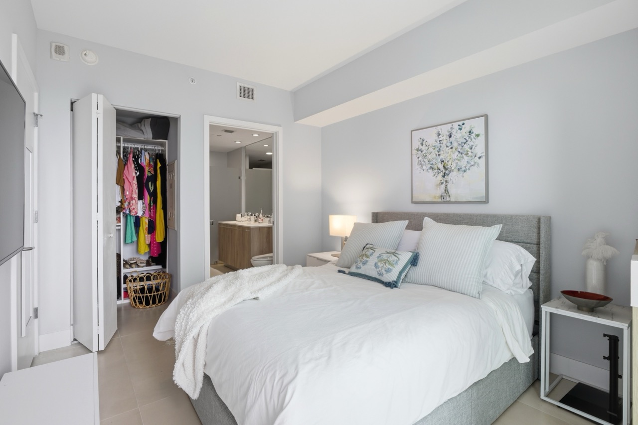 Bedroom interior showing a walk-in closet with colorful clothes and a grey bed.