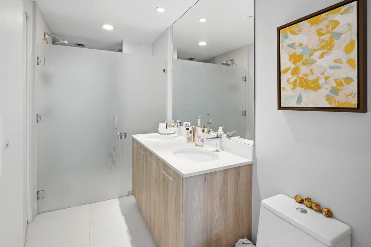 Modern bathroom with light wood double vanity, large mirror, and glass shower enclosure.