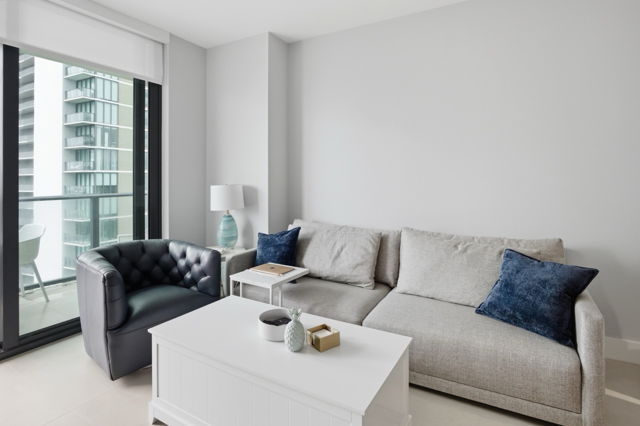 Living room setup with a grey sectional sofa, navy blue accent pillows, and white coffee table.
