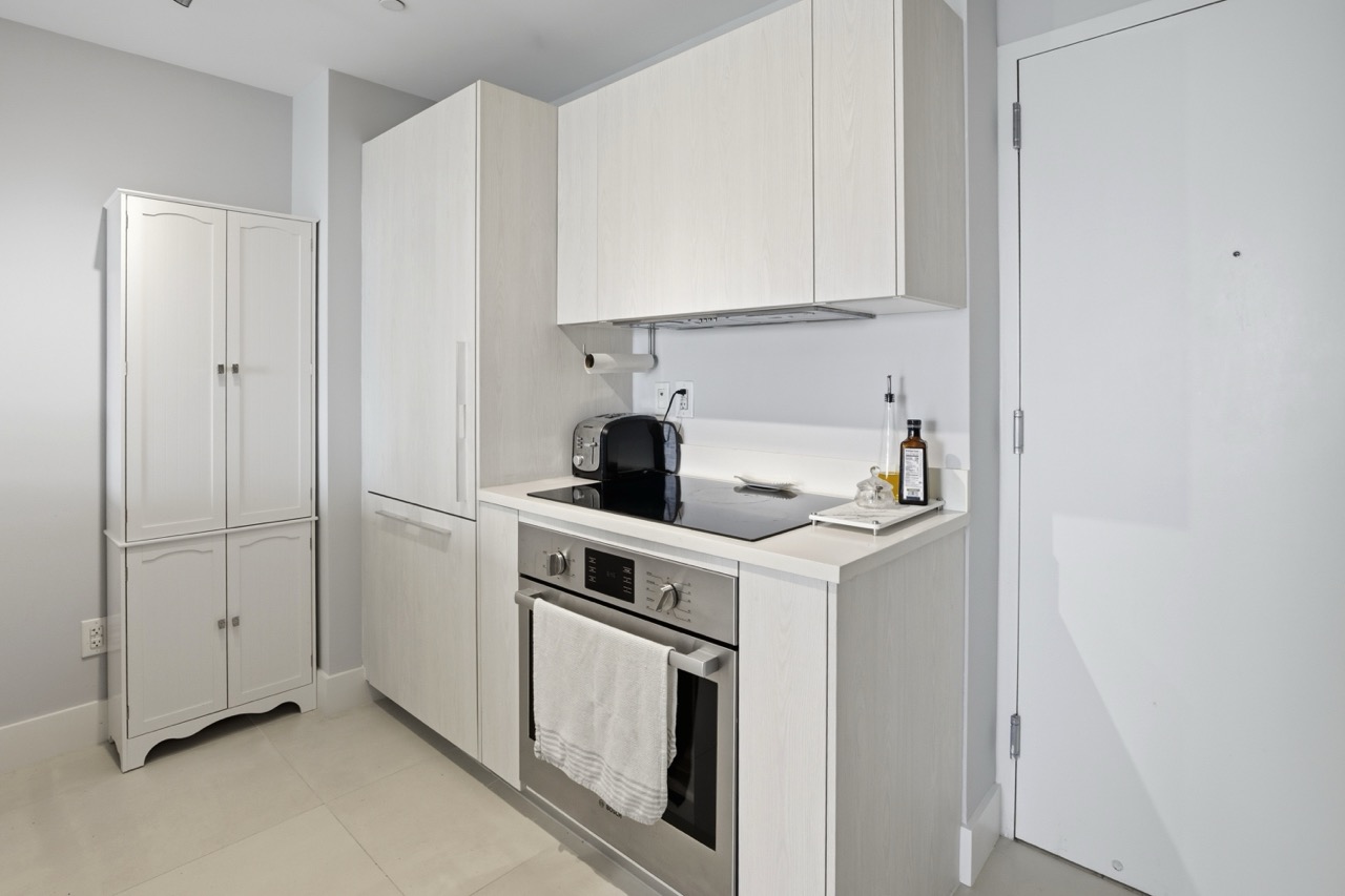 Compact modern kitchen with stainless appliances and white pantry.