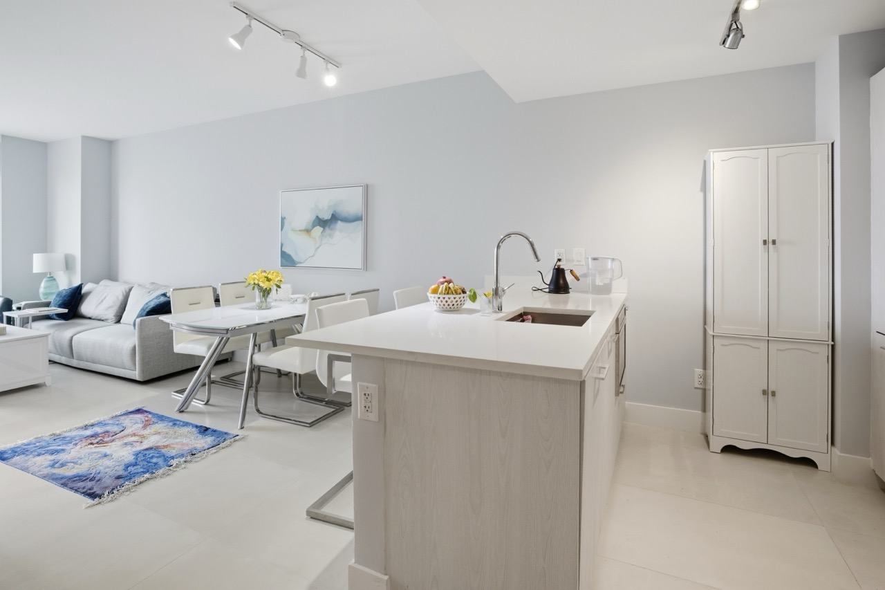 Bright open living space with kitchen island, dining table, and blue accent rug.