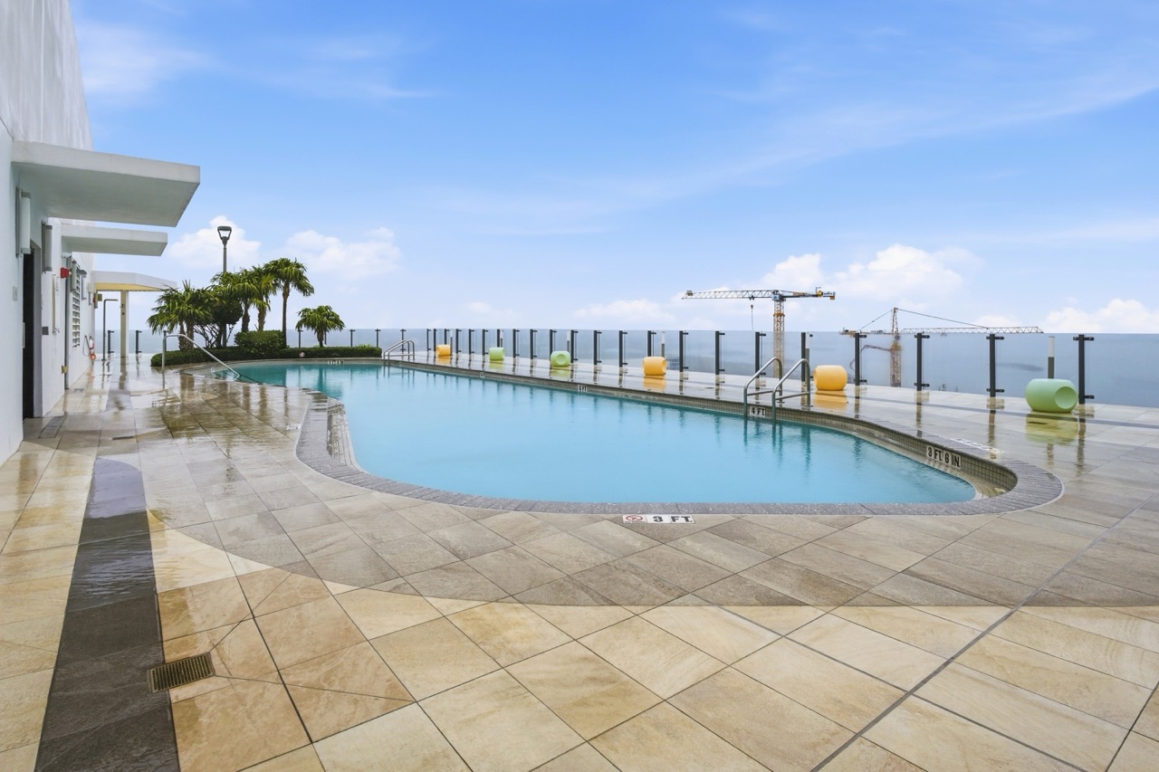 Outdoor rooftop swimming pool with lounge seating and bay views.